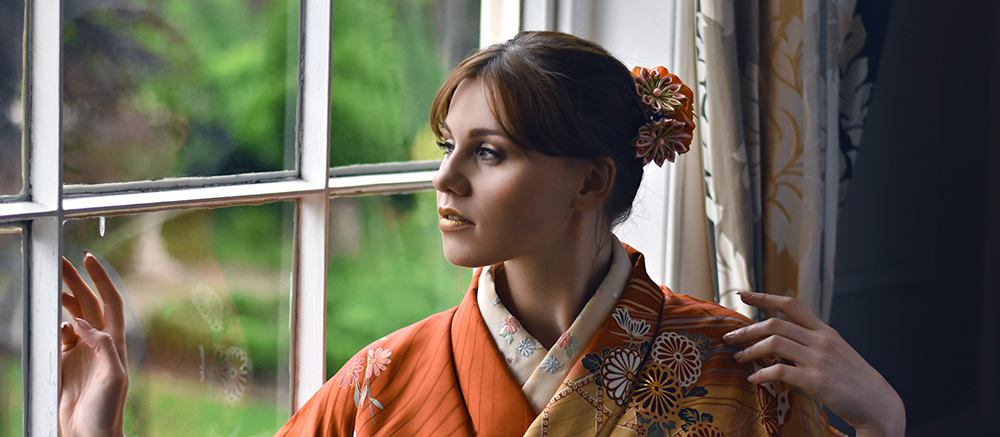Young woman in golden kimono sitting by a window